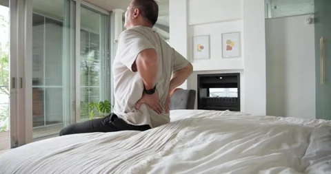 Senior Chinese man feeling back pain, sitting on bed edge and rubbing back near Stock Footage 337255033