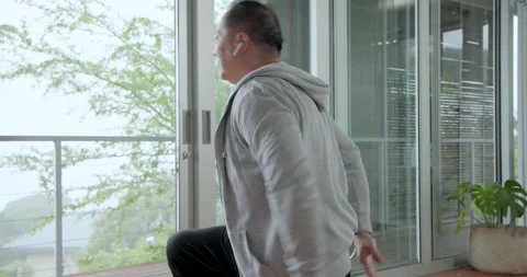 Senior Chinese man using earbuds, rotating, lunging, holding stretch on mat for Stock Footage 337254917