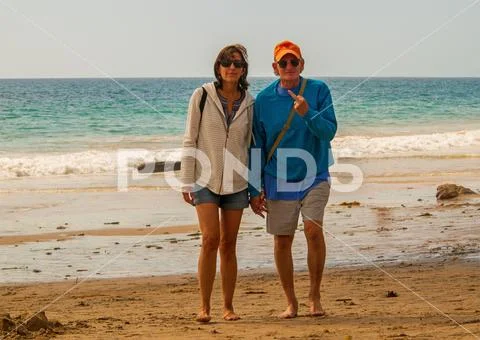 Senior citizen baby boomer male and female couple walking on the beach toward Stock Photos