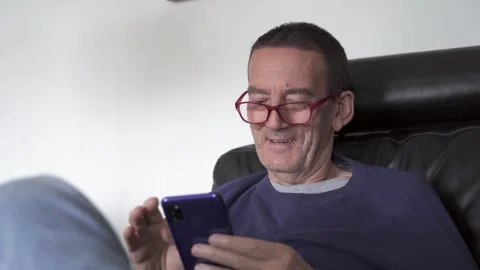 Senior citizen with glasses laughs while checking phone Stock Footage 290954265