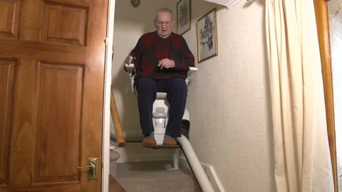 Senior Citizen man coming down stairs on Stair lift inside home - Chair Elevator Stock Footage 128514042