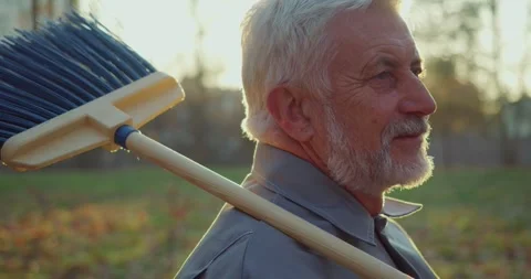 Senior concierge posing at park with broom on shoulder Stock Footage 254770318