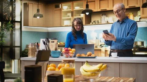 Senior couple checking smartphone apps in home kitchen with a relaxed smile Stock Photos