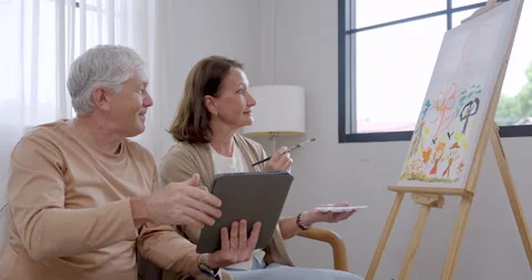 Senior couple compare tablet reference with canvas while woman holds brush Stock Footage 340169143