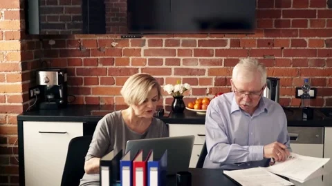 Senior couple comparing data on laptop and documents in the kitchen Stock Footage 101733477