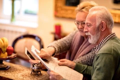 Senior couple having fun while reading newspaper and using tablet Stock Photos