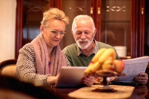 Senior couple having fun while reading newspaper and using tablet Stock Photos