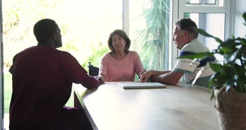 Senior couple holding hands after chat at dining table while caregiver fetching Stock Footage 342391836