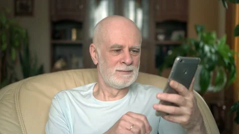 Senior couple at home. Husband using smartphone. Wife spying on her husband from Stock Footage 75043236