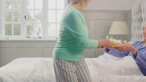 Senior Couple At Home With Woman Bringing Senior Man Breakfast In Bed On Tray Stock Footage