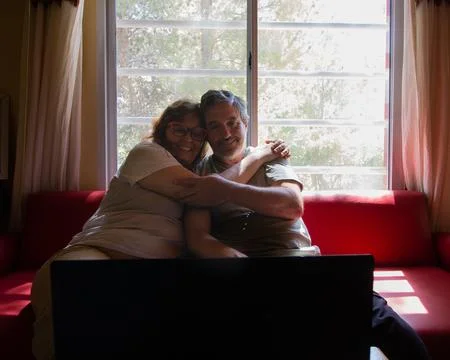 Senior couple hugging on sofa using laptop at home Stock Photos