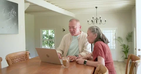 Senior couple leaning at dining table, woman pointing at laptop, man typing card Stock Footage 336059329