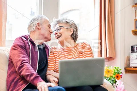 Senior Couple On Living Room Sofa Using Laptop