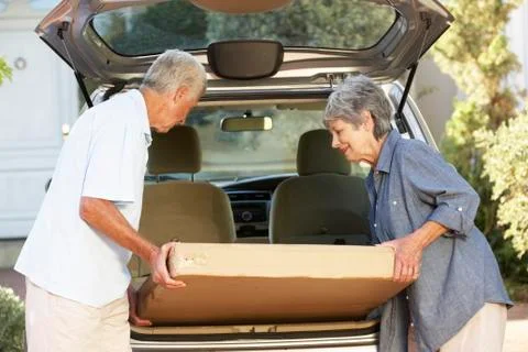 Senior Couple Loading Large Package Into Back Of Car Stockfoto's