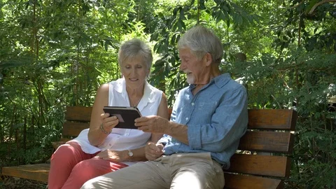 Senior couple looking at tablet computer in a park Stock Footage 91705786