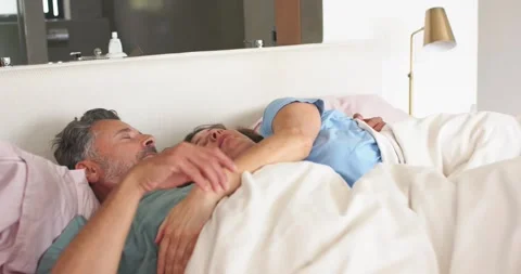Senior couple lying close in bed under comforter, man lifting arm, initiating Stock Footage 337625212
