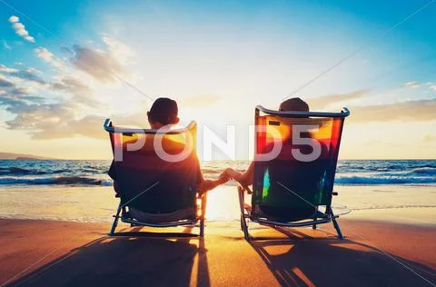 Senior couple of old man and woman sitting on the beach watching sunset Stock-Fotos