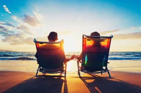 Senior couple of old man and woman sitting on the beach watching sunset Stock Photos