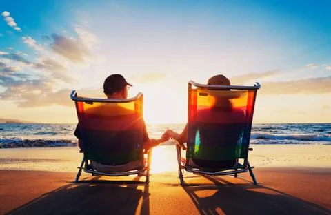 Senior couple of old man and woman sitting on the beach watching sunset Stock Photos