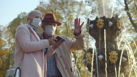 Senior couple in protective mask using headphones and smartphone having tour in Stock Footage 142202188