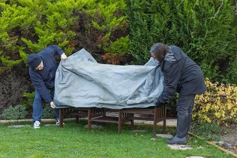 Senior couple pulling down winter cover to protect garden furniture Stock Photos