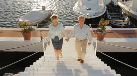 Senior couple running up steps towards camera by marina in sunset Stock Footage 43623007