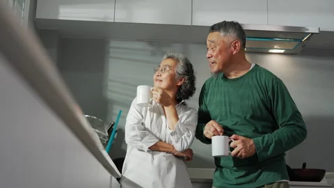 A senior couple shares laughter while enjoying their morning coffee together in Stock Footage 303708284