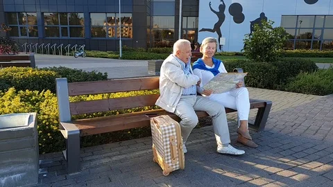 Senior couple sits with map on bench standing on park square Stock Footage 127182090