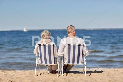 Senior couple sitting on chairs at summer beach Stock Photos