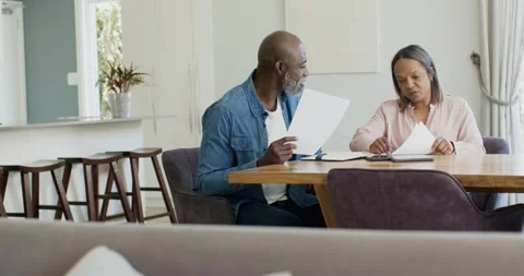 Senior couple sitting at dining table, man holding sheet initiating sorting Stock Footage 340612370