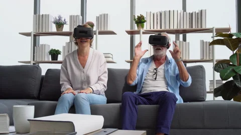 Senior couple sitting on sofa having fun with virtual reality glasses Stock Footage 162283681
