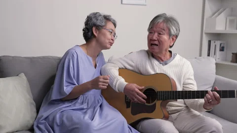 Senior couple sitting on the sofa while playing guitar and sings the songs. Stock Footage 221384834