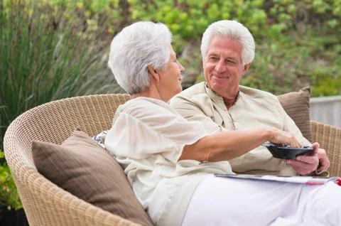 Senior couple sitting in a wicker couch eating food Stock Photos