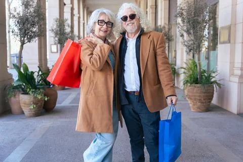 Senior couple smiling at camera while hugging and holding colorful shopping bags Stock Photos