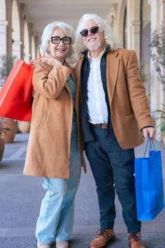 Senior couple smiling at camera while hugging and holding colorful shopping bags Stock Photos