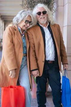 Senior couple smiling at camera while hugging and holding colorful shopping bags Stock Photos