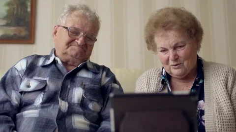 Senior couple in sofa using electronic tab. A cheerful senior couple having a Stock Footage 74359849