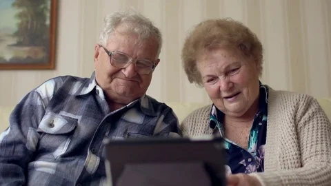 Senior couple in sofa using electronic tab. A cheerful senior couple having a Stock Footage 74360078