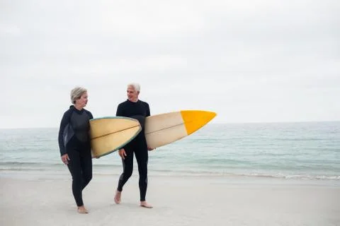 Senior couple with surfboard walking on the beach on a sunny day Stock Photos