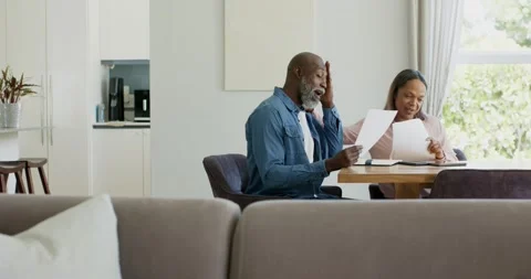 Senior couple at table high-fiving after finding news in papers, laughing, man Stock Footage 335747236