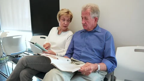 Senior couple talking and reading magazines, waiting in clinic waiting room Stock Footage 220408371