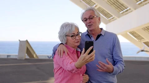 Senior couple talking during a video call standing outdoors Stock Footage 262108046