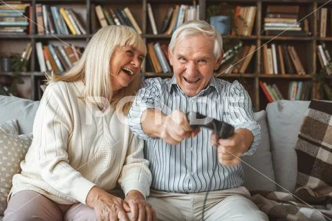 Senior couple together at home retirement concept sitting playing game laughing Stock Photos