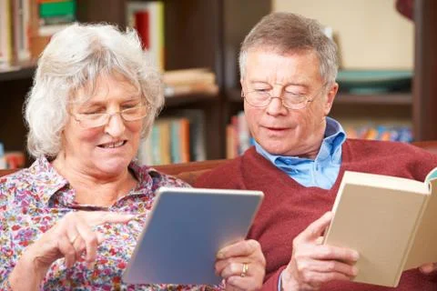 Senior Couple Using Digital Tablet And Reading Book Stock Photos