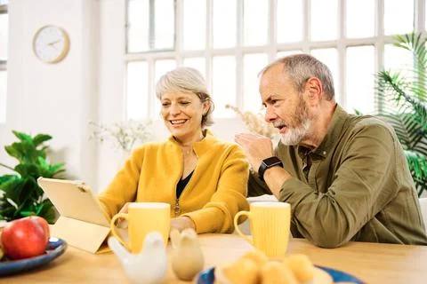 Senior couple using digital tablet at home having breakfast Stock Photos