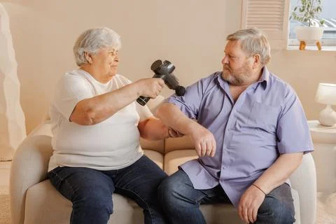 Senior Couple Using Percussion Massage Gun for Pain Relief and Wellness The.. Stock Photos