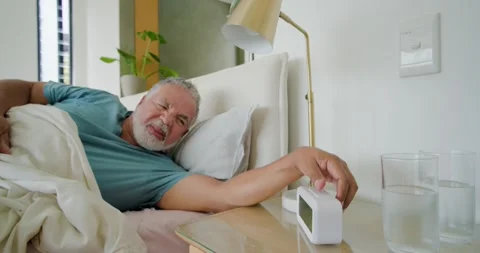 Senior couple waking in bed as digital clock ringing man reaching silencing Stock Footage 339416241