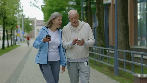 Senior couple is walking after the training and using their phone. Mature man is Stock Footage 225708141