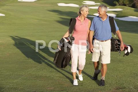 Senior Couple Walking Along Golf Course Carrying Bags Stock Photos