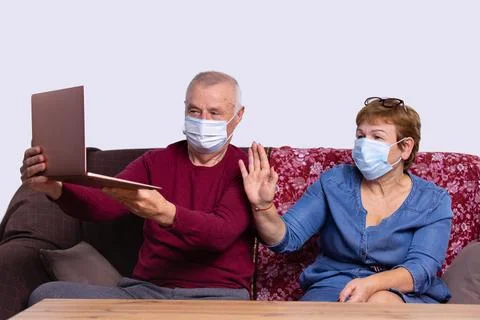 Senior couple waving while having a video call on laptop at home on sofa. Soc Stock-Fotos